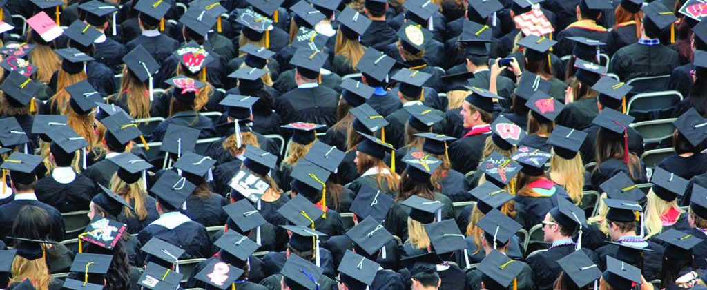 A crowd at a grauation ceremony, facing the same direction and wearing black graduation caps.