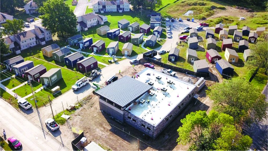 An aerial view of a small neighborhood of tiny homes, with a larger building in the foreground.