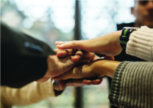 Five hands stacked on top of each other in a group huddle