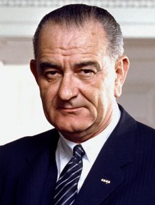 A portrait image shows Lyndon B. Johnson from the shoulders up. He is wearing a blue blazer, white collared shirt, and a blue tie with white stripes.