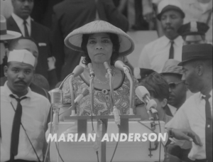 A black and white image shows Marian Anderson standing behind a podium, surrounded by a crowd. She is wearing a large hat, necklace, and dress.