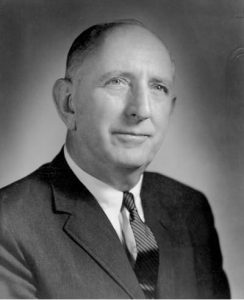 A black and white image shows a portrait of Richard Russell Jr wearing a suit and tie.