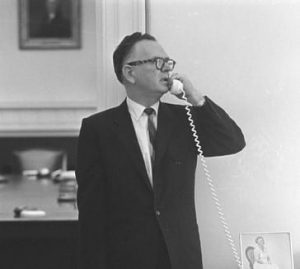 A black and white image shows Walter Jenkins in a suit and tie, speaking into a white phone.
