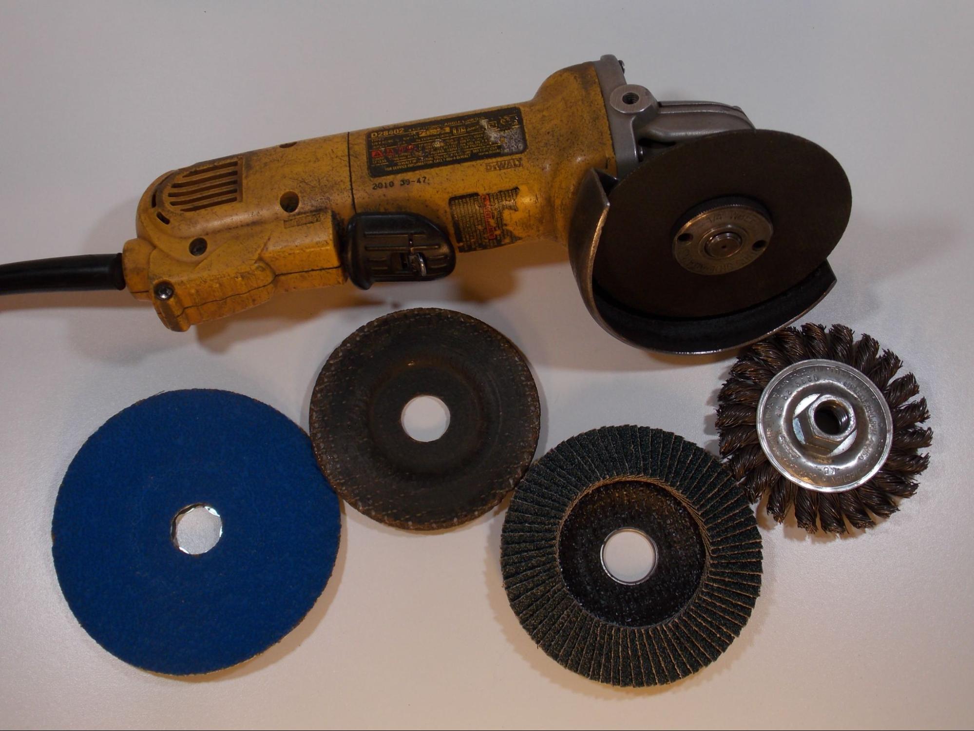 A common angle grinder. The tool has a threaded spindle at the head to which different abrasive discs can be mounted. The angle grinder is surrounded by four different examples of abrasive discs.