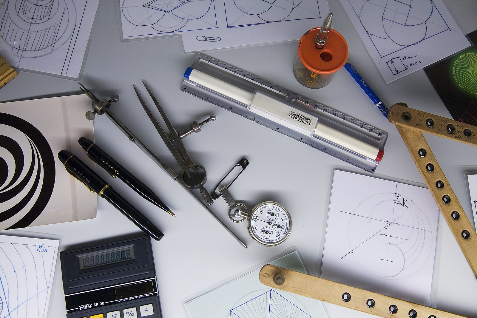 A desk with rulers, pens, compasses, and other layout tools, along with patterns that are being worked out.