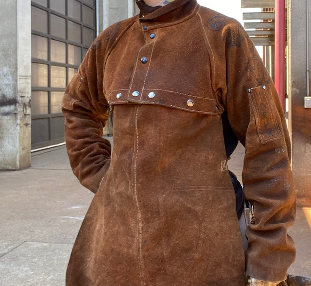 A person wearing a set of leather button-up welding sleeves and snap-on bib.