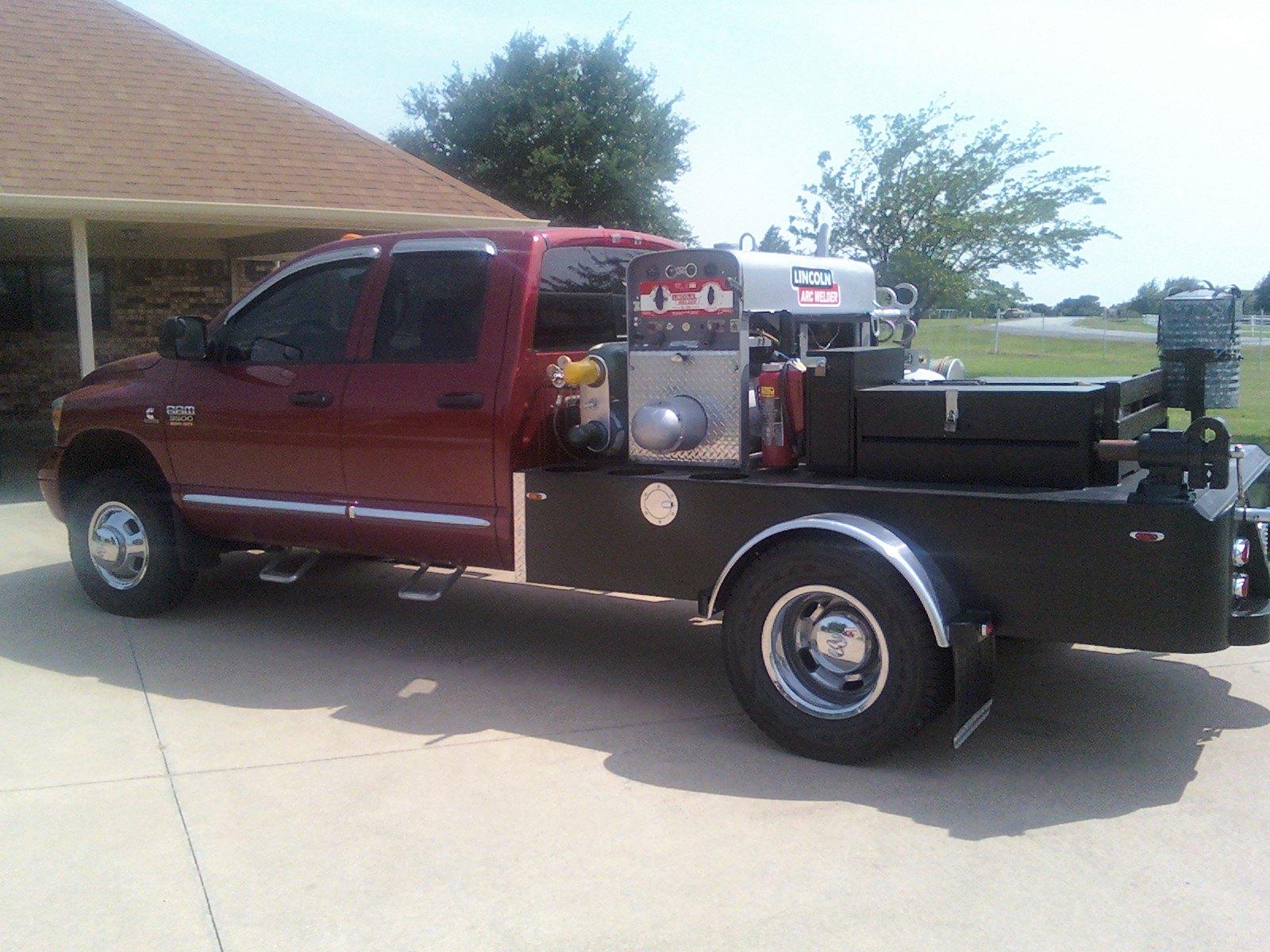 A pickup truck with a flatbed has a large generator welder and other equipment mounted on the bed.