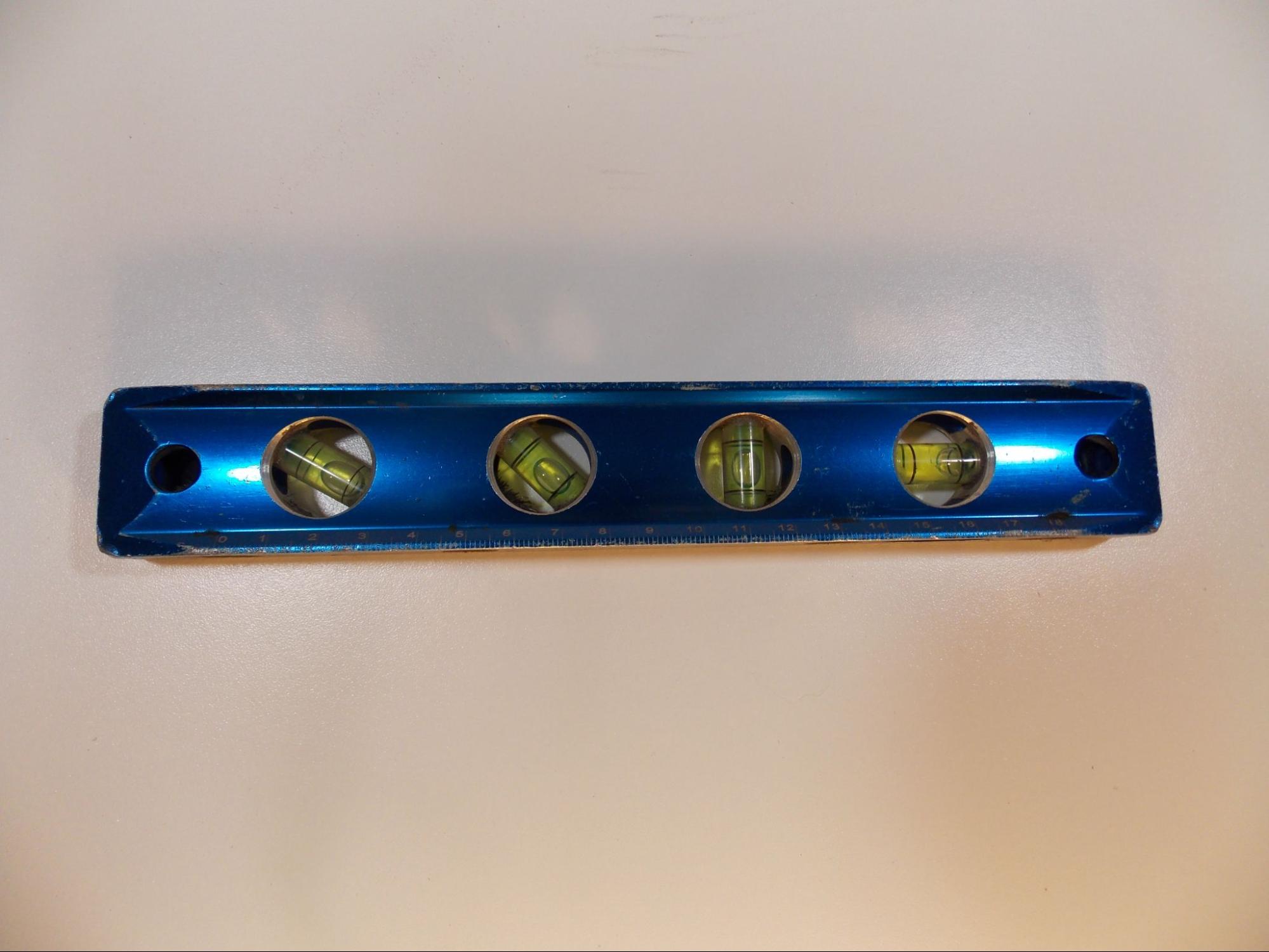A torpedo level with four cutaways that hold plastic tubes containing bright yellow liquid with a single air bubble in each. Marks on the tubes indicate where the bubbles should rest when the level is in the desired position to indicate four different angles with reference to the edge of the tool: from left to right they are 30 degrees, 45 degrees, 90 degrees (vertical), and 0 degrees (horizontal).