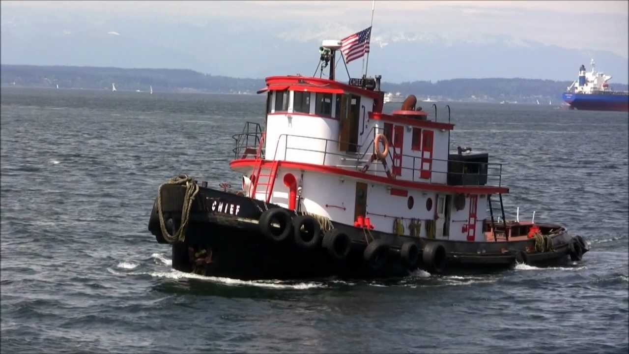 A tug boat with a black base, and a red and white cabin. In the background is a larger ship.