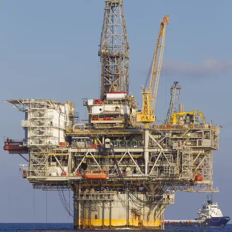 An offshore drilling platform. It has a large cylindrical base with an enormous scaffolding with cranes attached. A passenger ship is next to the platform on the right.