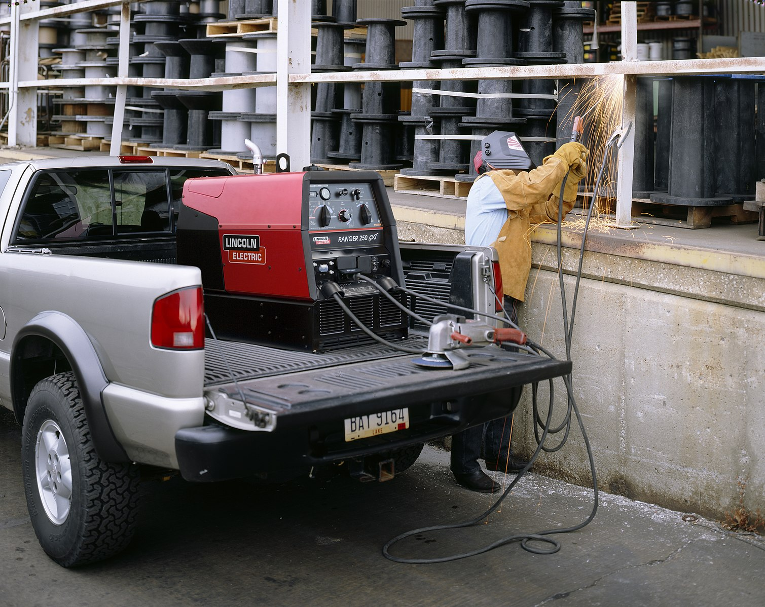 A welder repairs a handrail with SMAW, powered by an engine-driven welding machine in the back of a pickup truck.