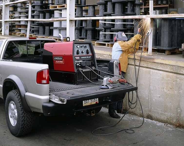 A welder performs SMAW on some railing using an engine-driven power source that is in the bed of a pickup truck.