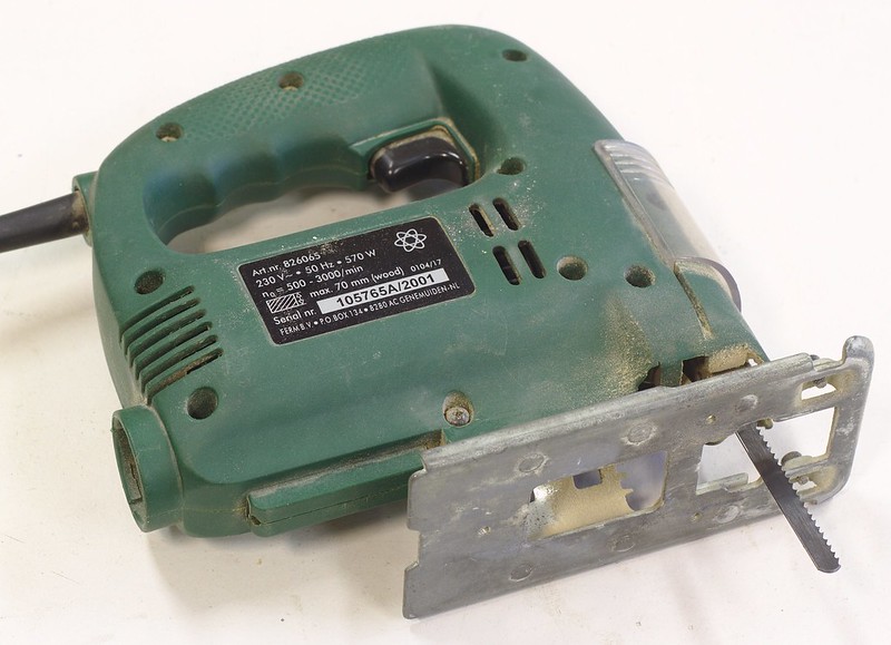 A typical jigsaw. This power tool has a small straight metal saw blade affixed to the bottom front of the tool. There is a metal foot at the bottom of the tool through which the saw blade moves up and down when the tool is on.