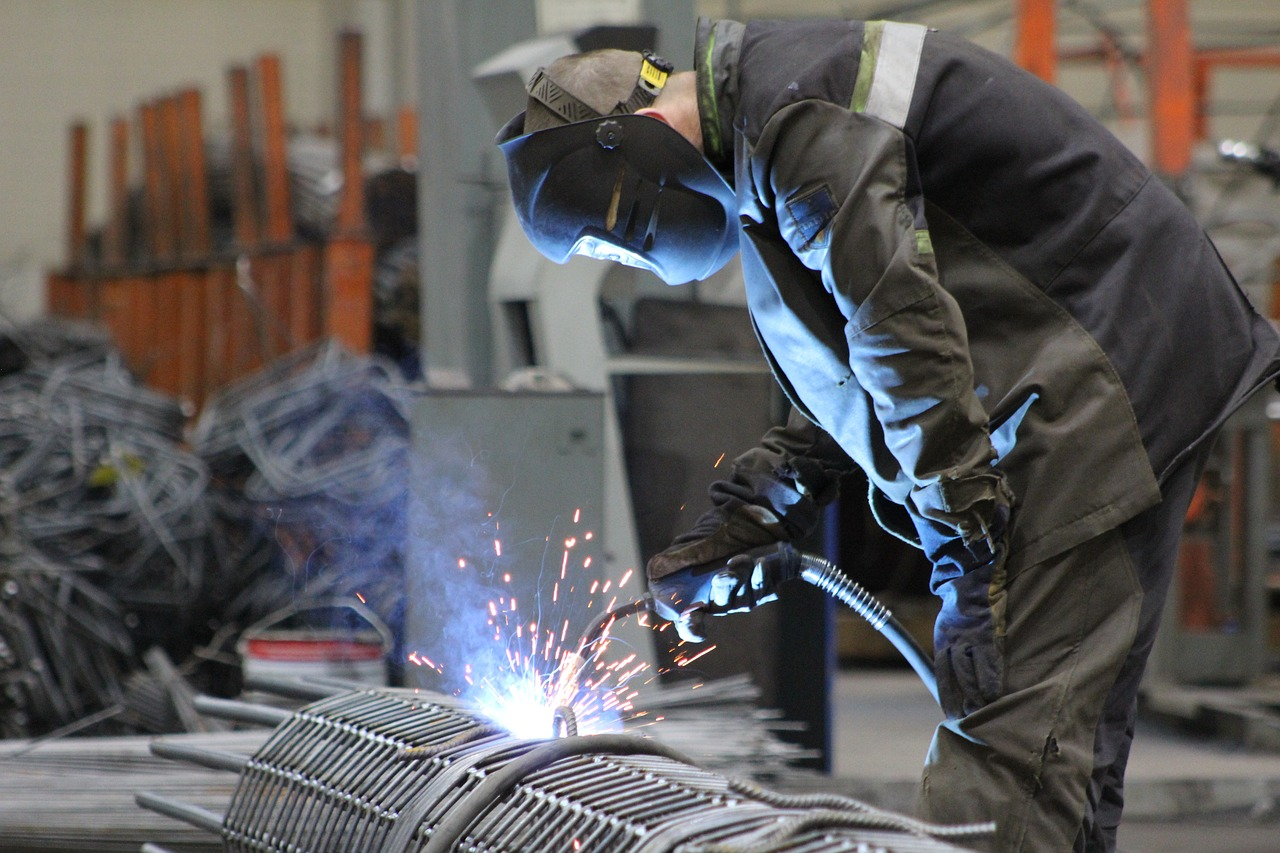 A man in full protective clothing, welds rebar with a wire feed welder, his clothes illuminated by the welding arc.