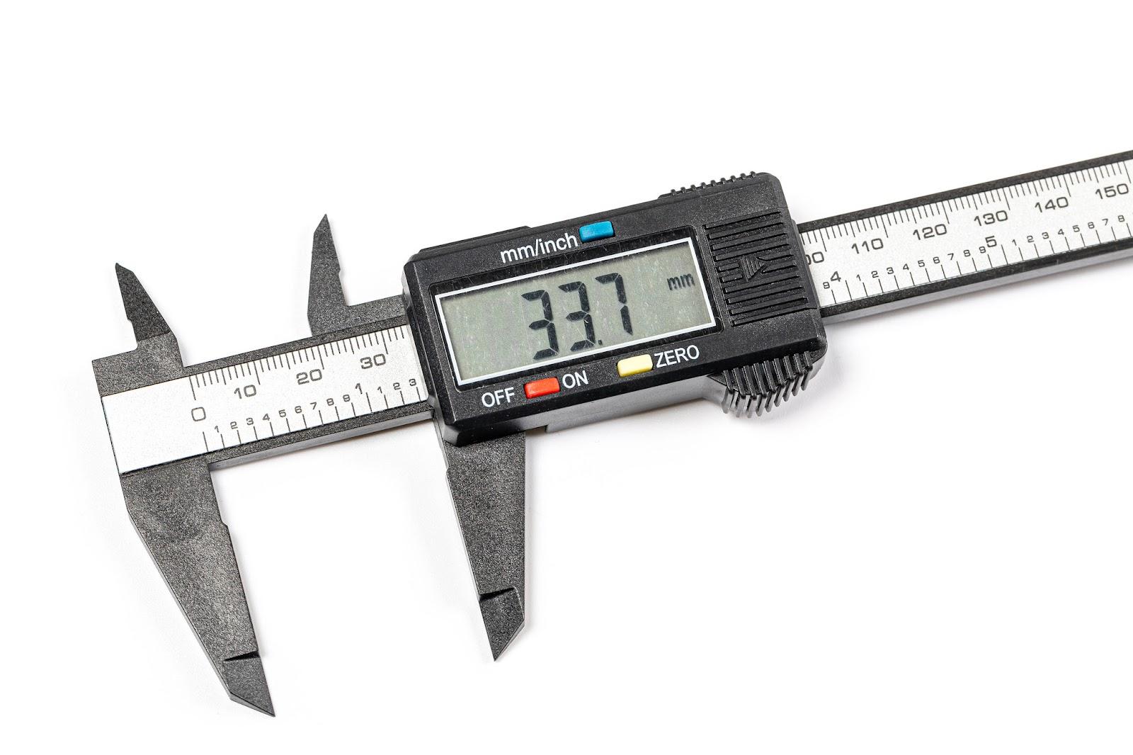 A set of digital calipers showing the bar with Imperial and metric scales, the outside and inside jaws, and the digital indicator attached to the sliding lower jaws. The calipers are open, and the digital display reads 33.7 milimeters.
