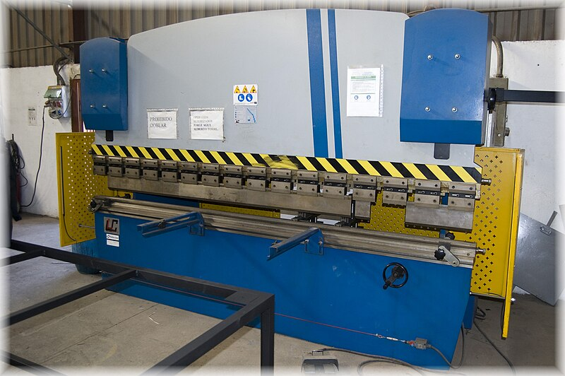 A machine used to bend sheet metal. The machine is rectangular, about six feet tall and ten feet wide, with a horizontal opening in the middle. The top part of the machine is made to move toward the bottom part like a set of jaws. The space between the top and bottom is where preshaped dies can be placed to bend metal to a specific angle or radius. The yellow parts of the machine are guards which are set to the sides to keep body parts away from the jaws when in operation.