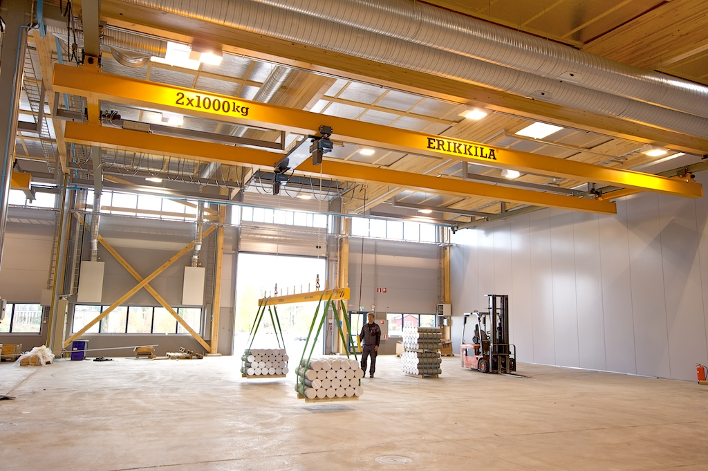 An empty building that has an overhead bridge crane lifting a load of metal weights.