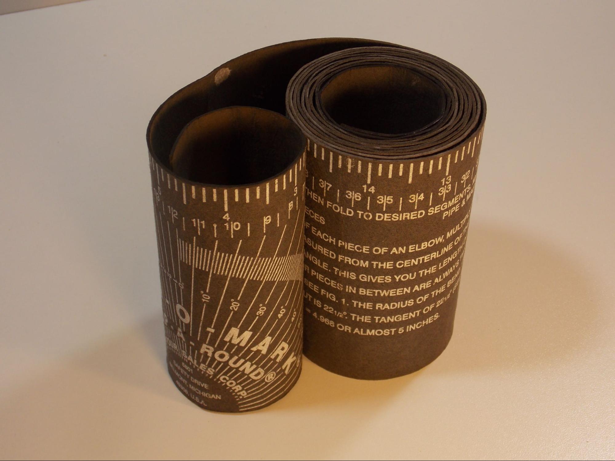 rolled up pipe wrap, which is a long strip of pliable cardboard with the Imperial measurement scale printed on the top edge and a 180 degree scale presented on the flat face of the tool.