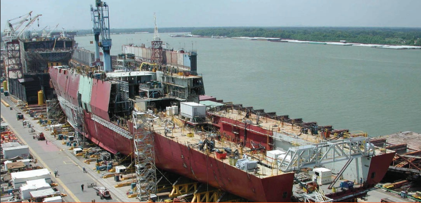 A large, red, steel ship is being built in a in dry dock.
