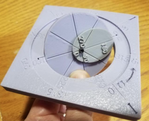 The image depicts a hand-held orbital element model, often referred to as a "whiz wheel," designed to aid students in visualizing orbits. This 3D-printed wheel serves as a portable educational tool, allowing students to interactively explore orbital elements and better understand the dynamics of celestial motion. While not as large as a full-scale orbital demonstrator, the whiz wheel offers a practical and accessible means for students to grasp fundamental astrodynamics concepts. Its design likely includes various components representing key orbital parameters, providing a hands-on learning experience in a more compact form.