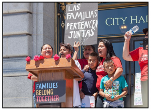 Photograph: Protesters with Causa Justa / Just Cause speak on the steps of San Francisco City Hall for a "Families Belong Together" rally. One holds a sign reading "Las Familias Pertenecen Juntas"