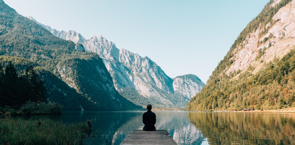 A person sitting on a dock surrounded by mountains