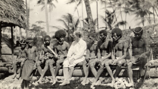 Bronislaw Malinowski sitting on a log with Trobriand Islanders