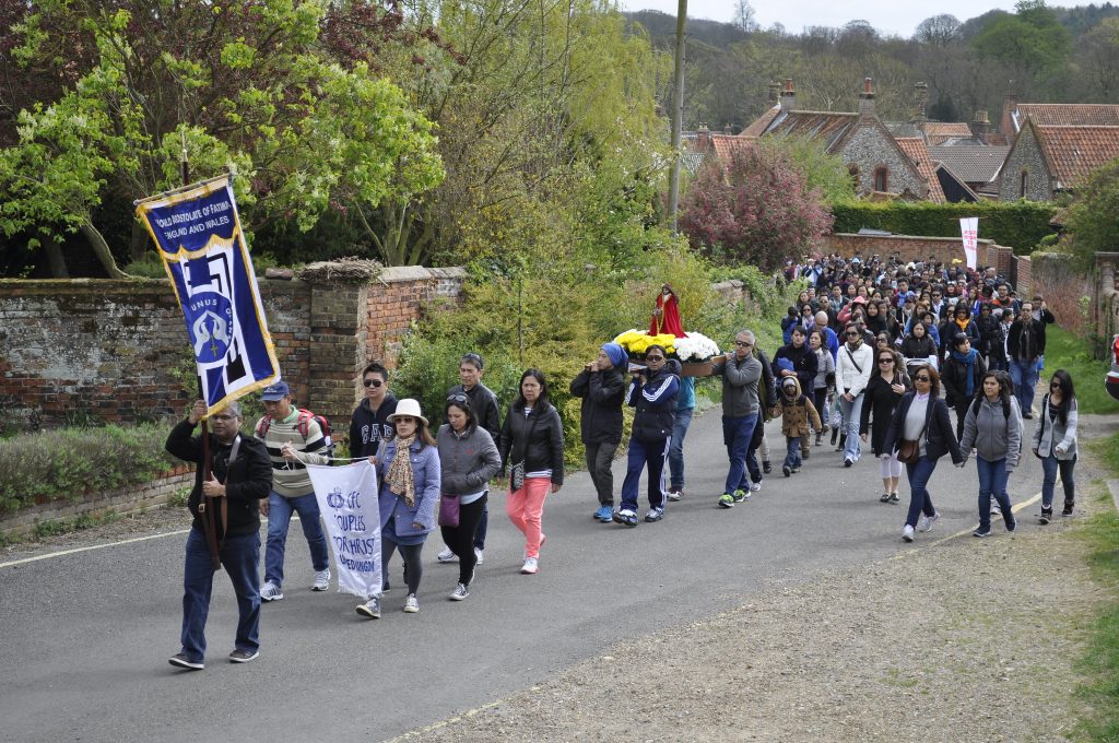 People walking in a procession through town, holding a banner and statuette