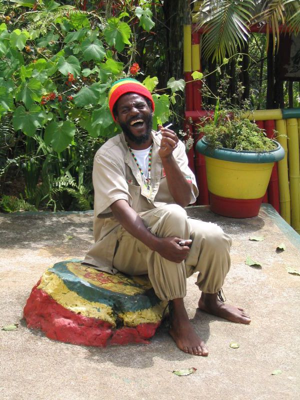 Rastafarian man sitting on rock and holding ganja