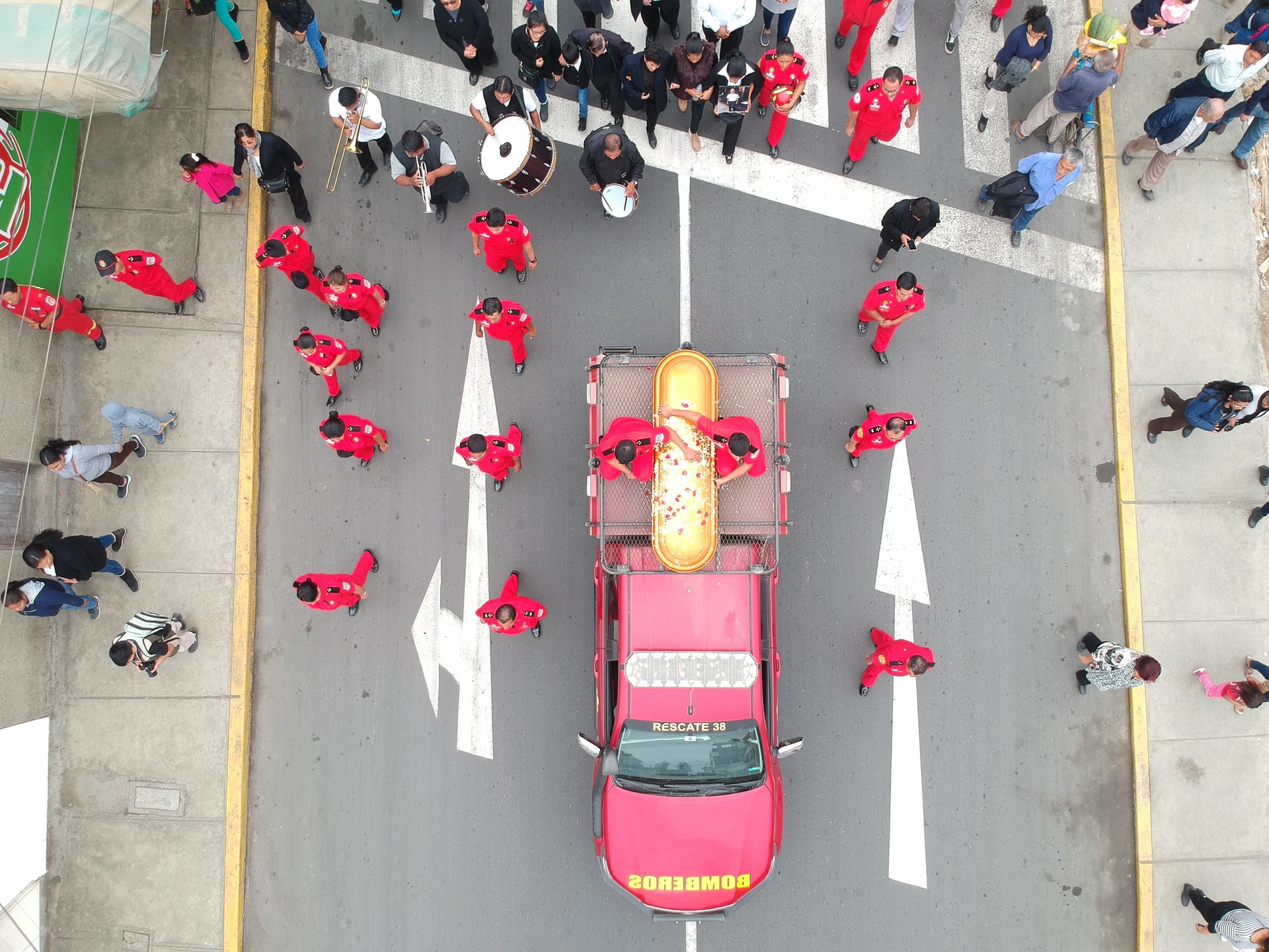 A funeral procession in a street, looking down on a car and people dressed in red.